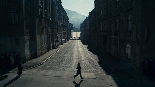 A mono image of a street in shadow with a lone figure walking.