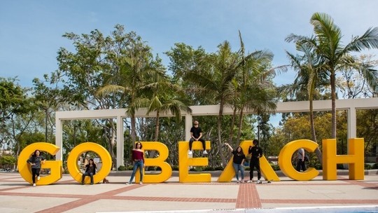 Students standing in front of a large yellow beach sign