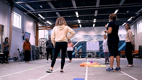 Eight people stand in a circle in a sports hall.