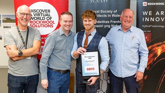 Drew Dennehy, a young man with blond hair wearing a shirt and tie under a dress waistcoast, holds his BSc Architecture and smiles broadly; he's standing between three older men, all smiling, including Architecture programme director Ian Standen.