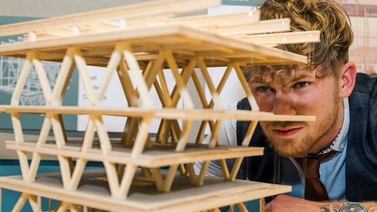 Drew Dennehy crouches down to view the criss-cross wooden frame of his design at eye level.
