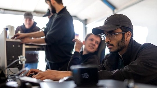 Wearing a baseball hat and glasses, Ragulan types on a keyboard, looking towards a screen with a look of concentration.