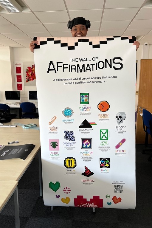 Summer Davies holds up a long banner called The Wall of Affirmations that includes fourteen graphics in a retro-pixellated style above titles such as Organised Mess and The Power of Music.