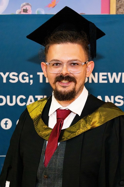 A happy, smiling graduate standing proudly, dressed in his cap and gown at graduation..