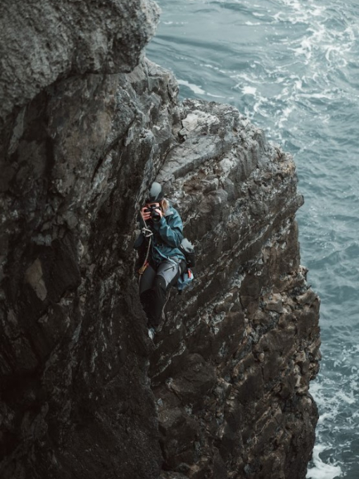 A person climbing a cliff overhanging the sea