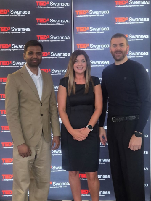 Three people standing against a branded backdrop.