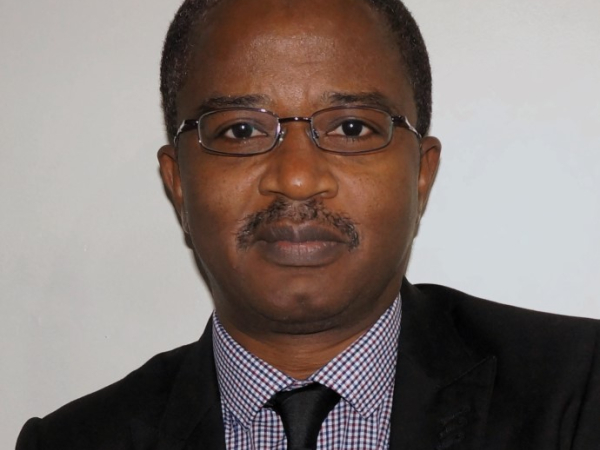 Wearing a suit and glasses, Dr Aliyu Sambo looks straight at the camera.