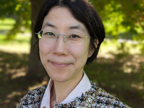 Dr Katherine Ngo smiles towards the camera on a sunny day with a tree in leaf behind her.