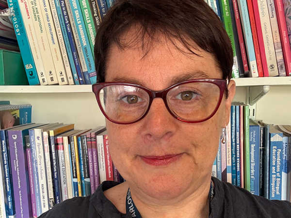 Wearing glasses and with short dark hair, bookshelves behind her, Alison Rees Edwards looks directly into the camera.