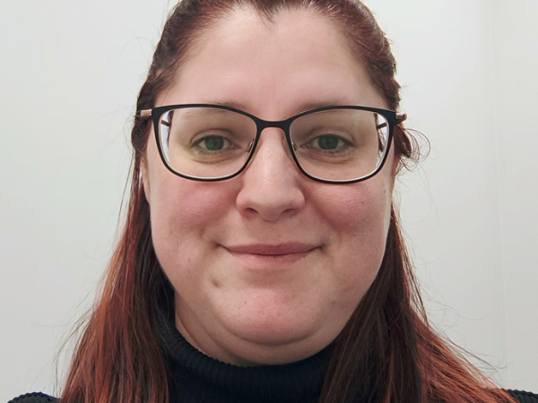 Wearing glasses and with long read hair, Natasha Young smiles towards the camera.