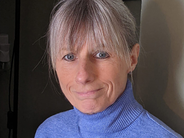 Wearing a cornflower blue polo neck, Sue Ainsworth looks towards the camera. 
