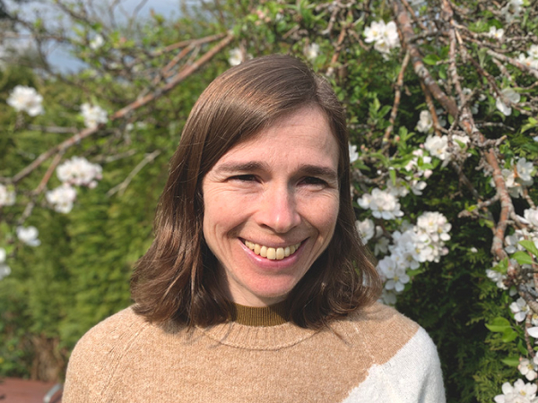 Dr Ffion Jones smiles in front of a hedge and a branch of apple blossom.