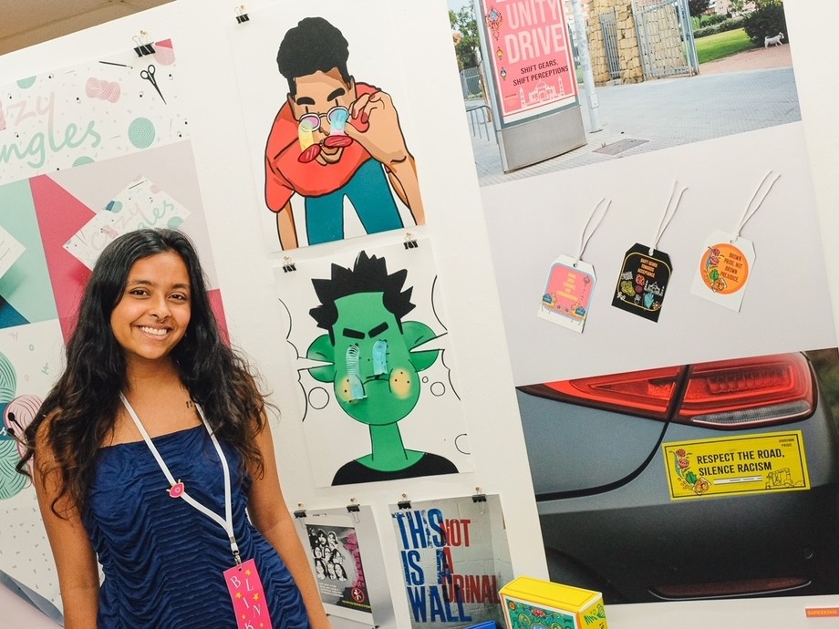 A smiling student standing in front of her colourful work.