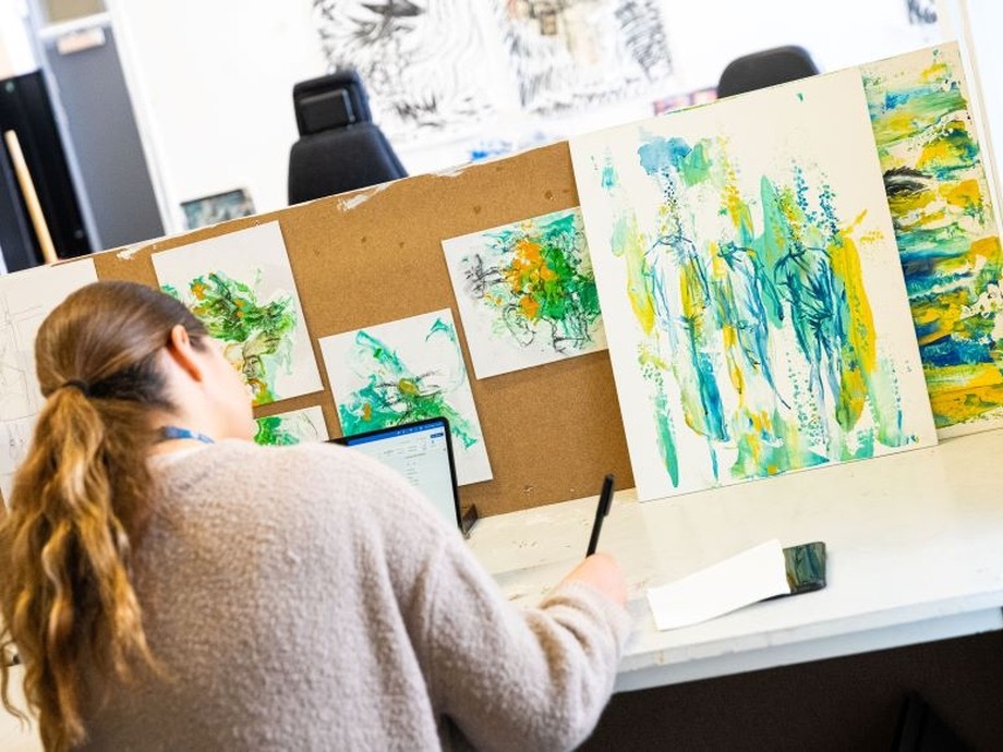 A student working at a desk surrounded by art work.