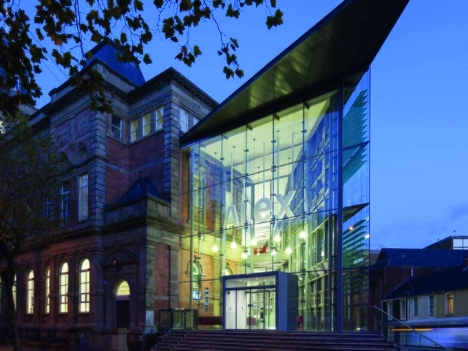 Image of UWTSD Alex building with a glass entrance with ALEX in white letters at dusk