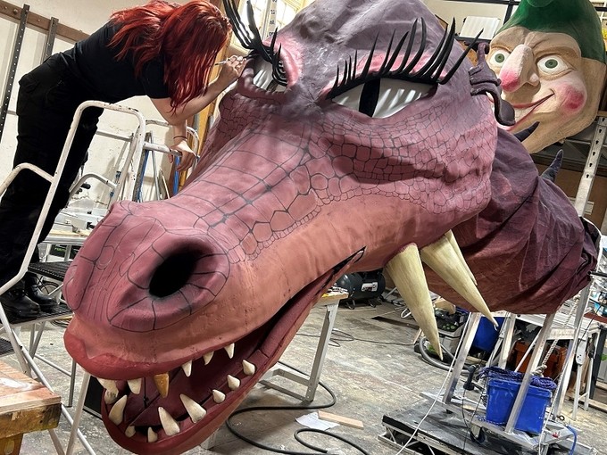 A woman on a stepladder adds the finishing touches to a giant red dragon head.