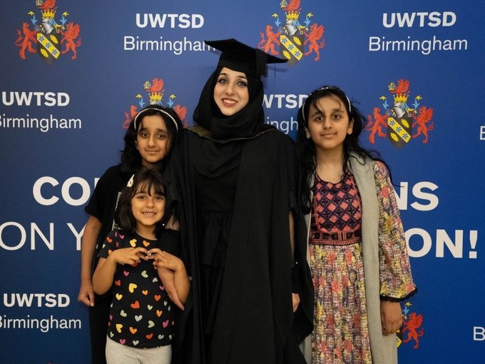 Madiha Hassan yn llawn balchder mewn cap a gŵn gyda’i thri phlentyn, pob un ohonynt yn gwenu, wrth ddathlu ei chyflawniad ar ddiwrnod graddio.