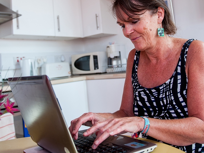 Person sitting down using a laptop with kitchen appliances in the background