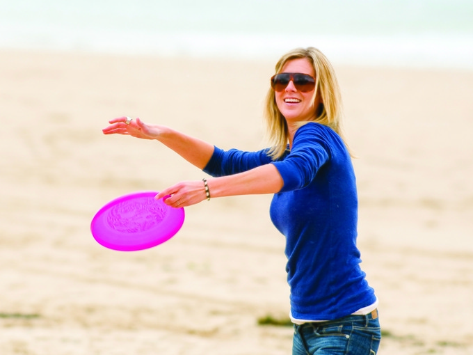 Myfyriwr ar draeth Abertawe yn taflu ffrisbi