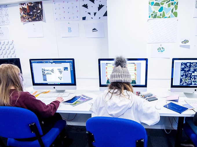 Three students creating designs on Apple Mac computers.