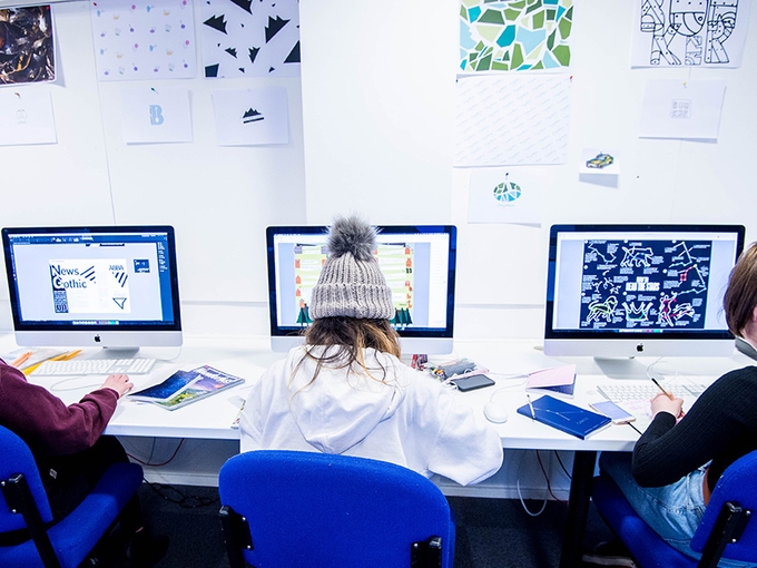 Tri myfyriwr yn creu dyluniadau ar gyfrifiaduron Apple Mac.
