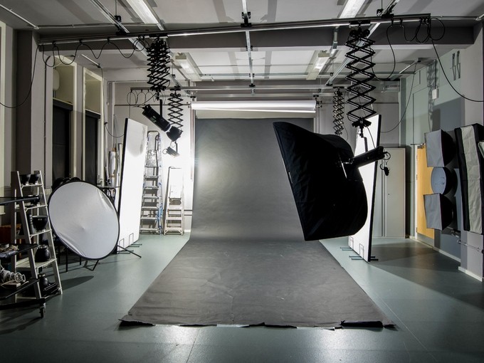 A photography studio with movable overhead lights, screens, and a long roll of black fabric spread across the floor.