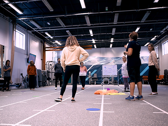 Eight people stand in a circle in a sports hall.