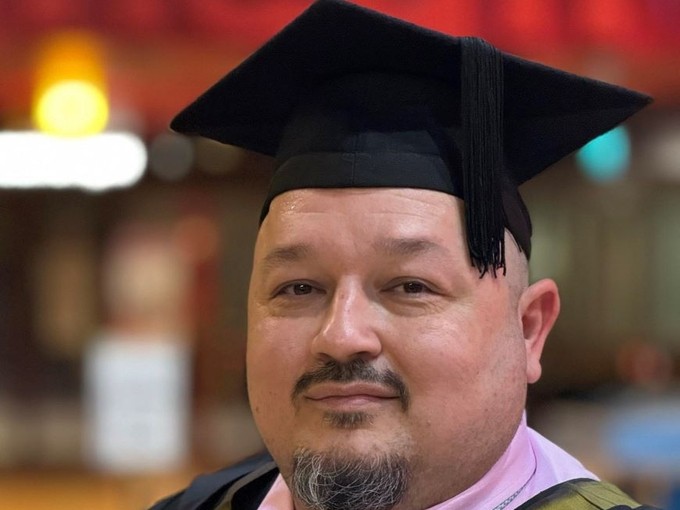 A happy, smiling graduate standing proudly, dressed in his cap and gown at graduation..