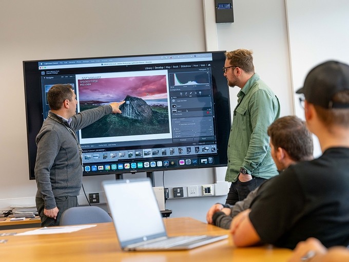 Brett Aggersberg yn tynnu sylw at fanylyn ar fonitor mawr iawn sy’n dangos llun o dŷ to gwellt hynafol yn Adobe Lightroom Classic.