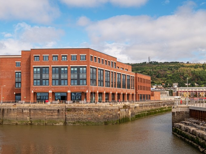 The old tidal basin and the red-brick IQ Building in the foreground; the wooded slope of Kilvey Hill occupies the background.