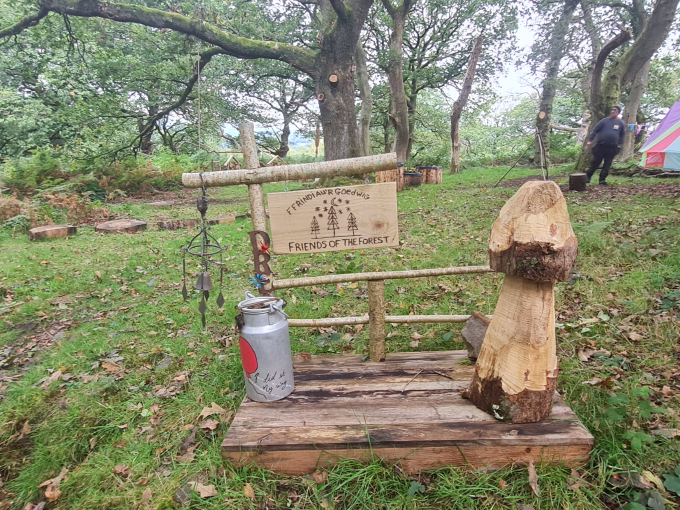 a wooden sign saying 'friends of the forest', wood cut into the shape of a mushroom, small milk churn