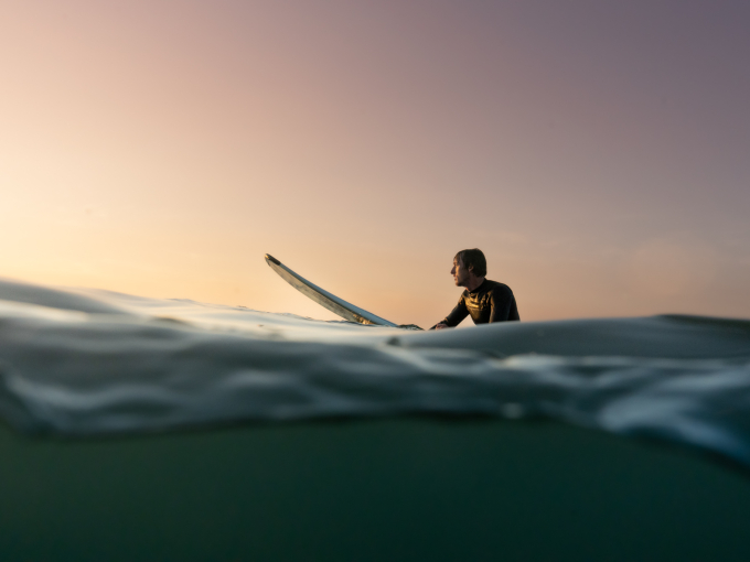 A person on a surf board in the sea looking at a sunset