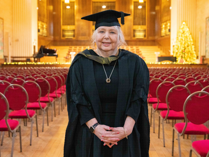 A similing female in academical dress stood in front of a stage