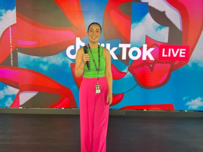 woman holding a microphone in front of backdrop that's branded 'TikTok Live'
