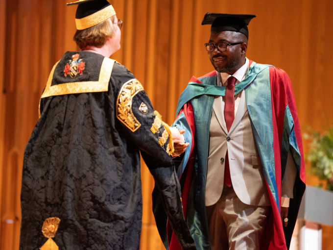 Charles Okeyia crossing graduation stage shaking hand of Vice Chancellor