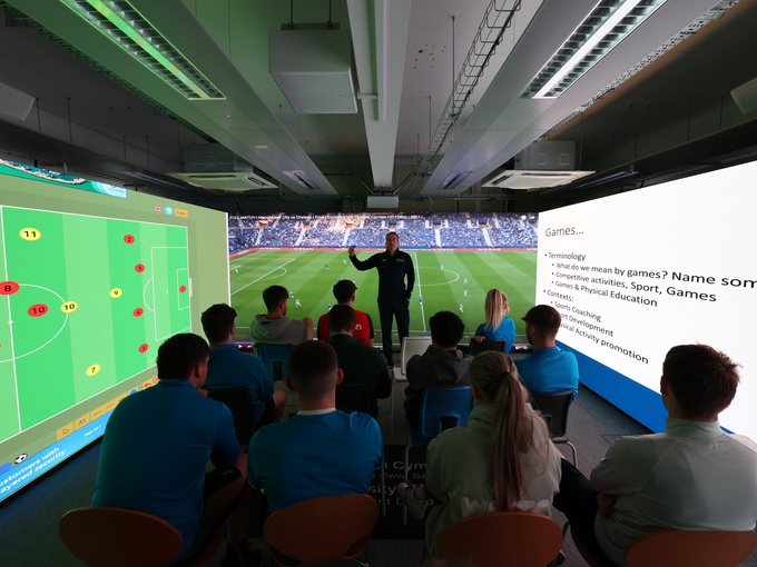 immersive room full of students watching sports on screen