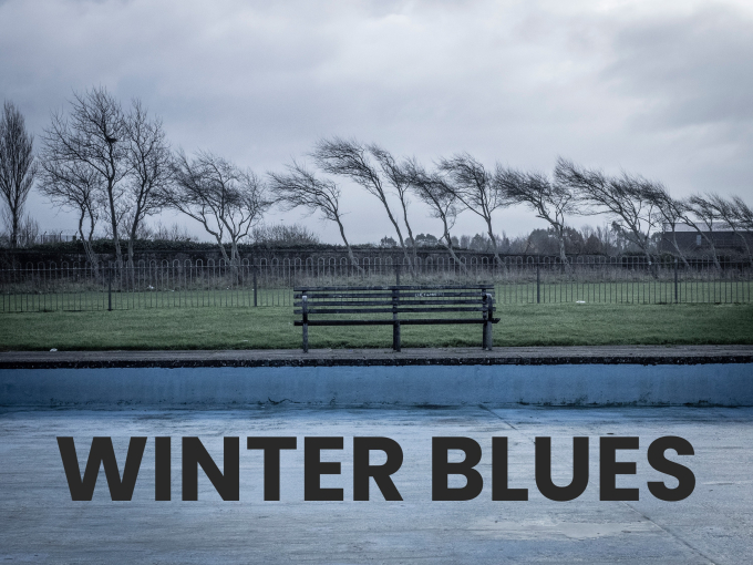 An empty bench on a windy, gloomy day with words 'Winter Blues'