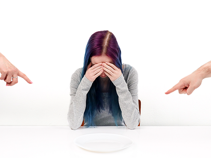 a person sitting down with hand on head looking at a plate and people pointing at the plate