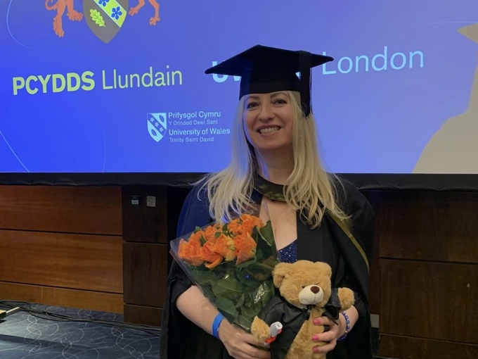 A woman graduating holding flowers and teddy bear