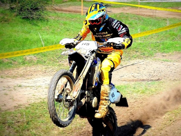 A motorbike rider in yellow and black protective gear doing a wheelie on a dirt track.