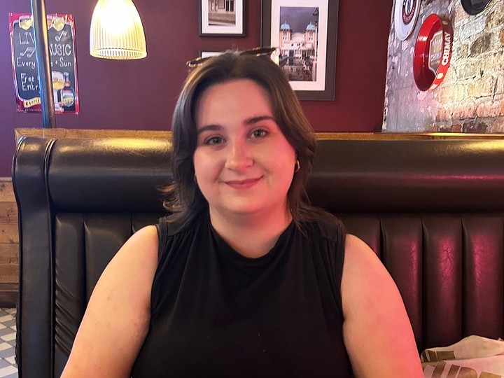 Rebecca Hodgson sits in a booth in a bar and smiles towards the camera.