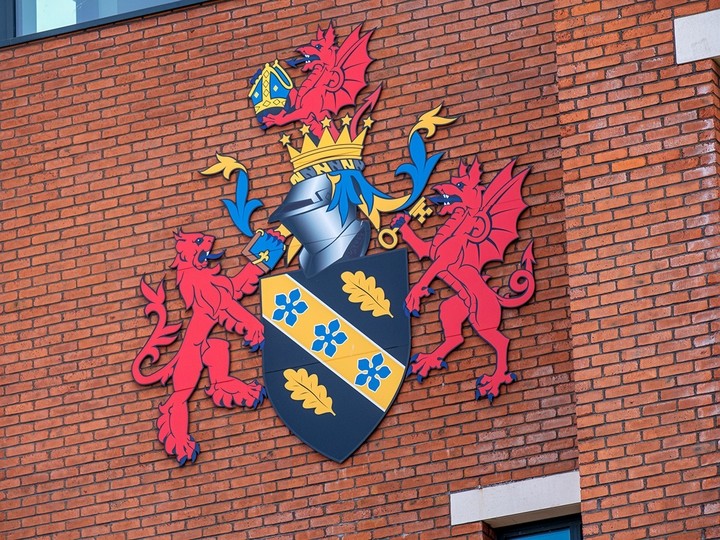The UWTSD coat of arms fixed to a modern wall of red brick.