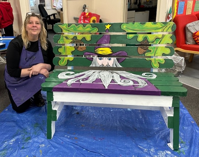 MA Illustration student Karen McRobbie kneeling down next to one of the benches created as part of Prosiect 23.