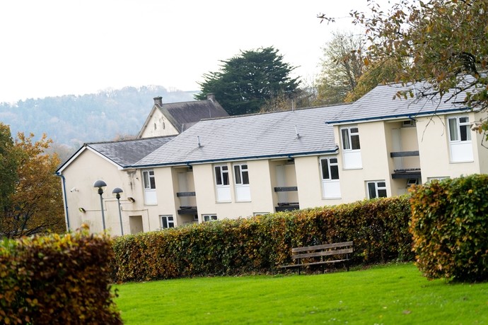 View across garden of Carmarthen halls of residence with park bench in foreground.
