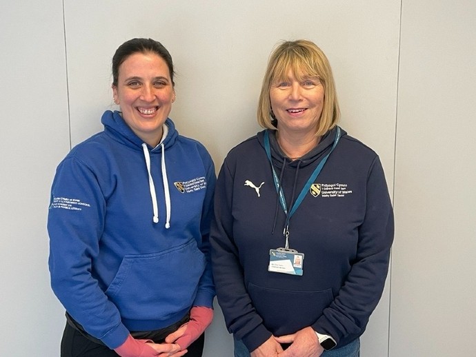 Beca Lyne-Pirkis and Chris Cashin wearing blue UWTSD hoodies and smiling.