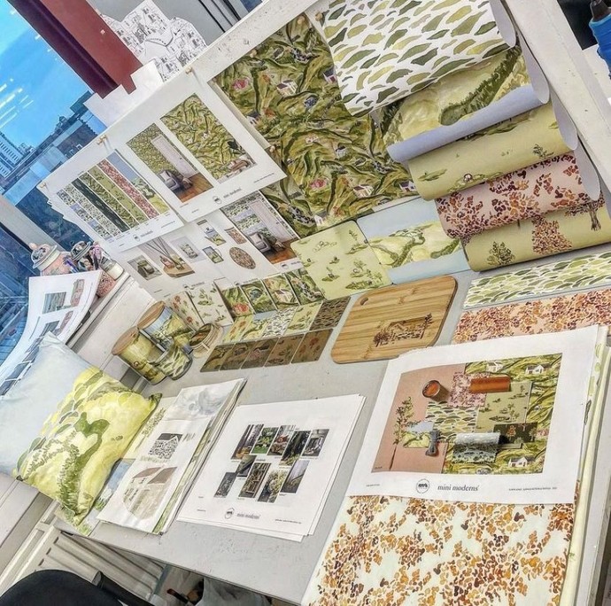 Ellie Jones's desk at Swansea College of Art; on the desk there are samples of wallpapers and textiles as well as several mood boards.