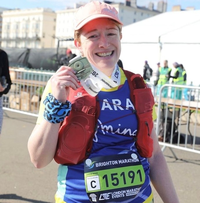 Laura Hopkinson, sy’n flinedig ond yn hapus ar ôl gorffen Marathon Brighton, yn gwisgo ei medal gyda balchder.