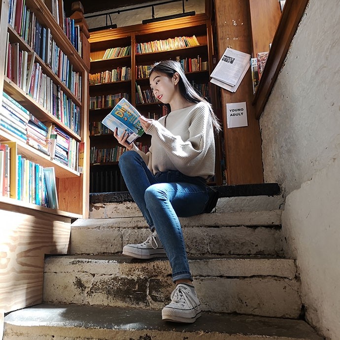 Yueyao Hu sitting reading on a flight of bare stone steps in a bookshop.