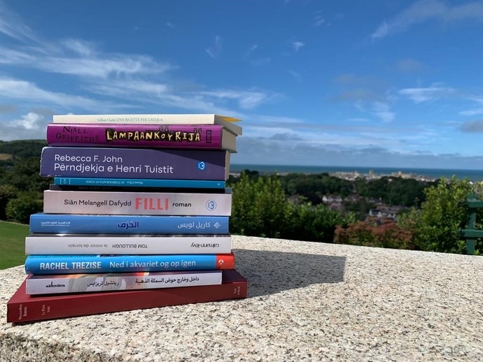 Books stacked on a wall with fields and blue sky in the background