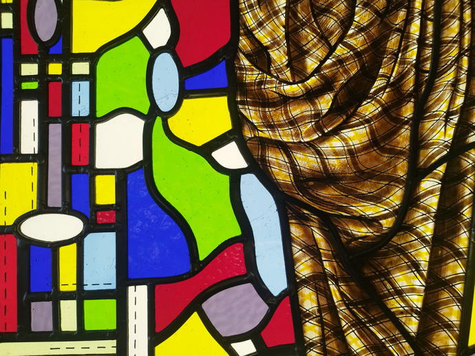 Pieces of stained glass in primary colours divided by black cames; half the glass is covered by a thin piece of chequered cloth. 